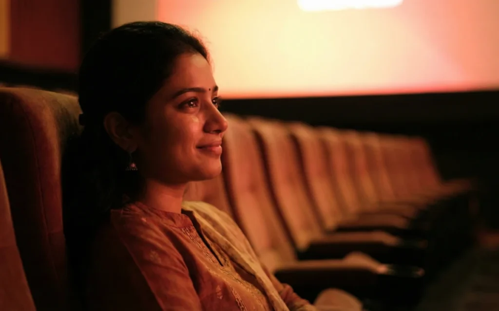 మందగించిన వెలుతురులో థియేటర్ సీట్లో కూర్చుని, కళ్లలో మెల్లని తడితో కథలో లీనమైన యువతి.